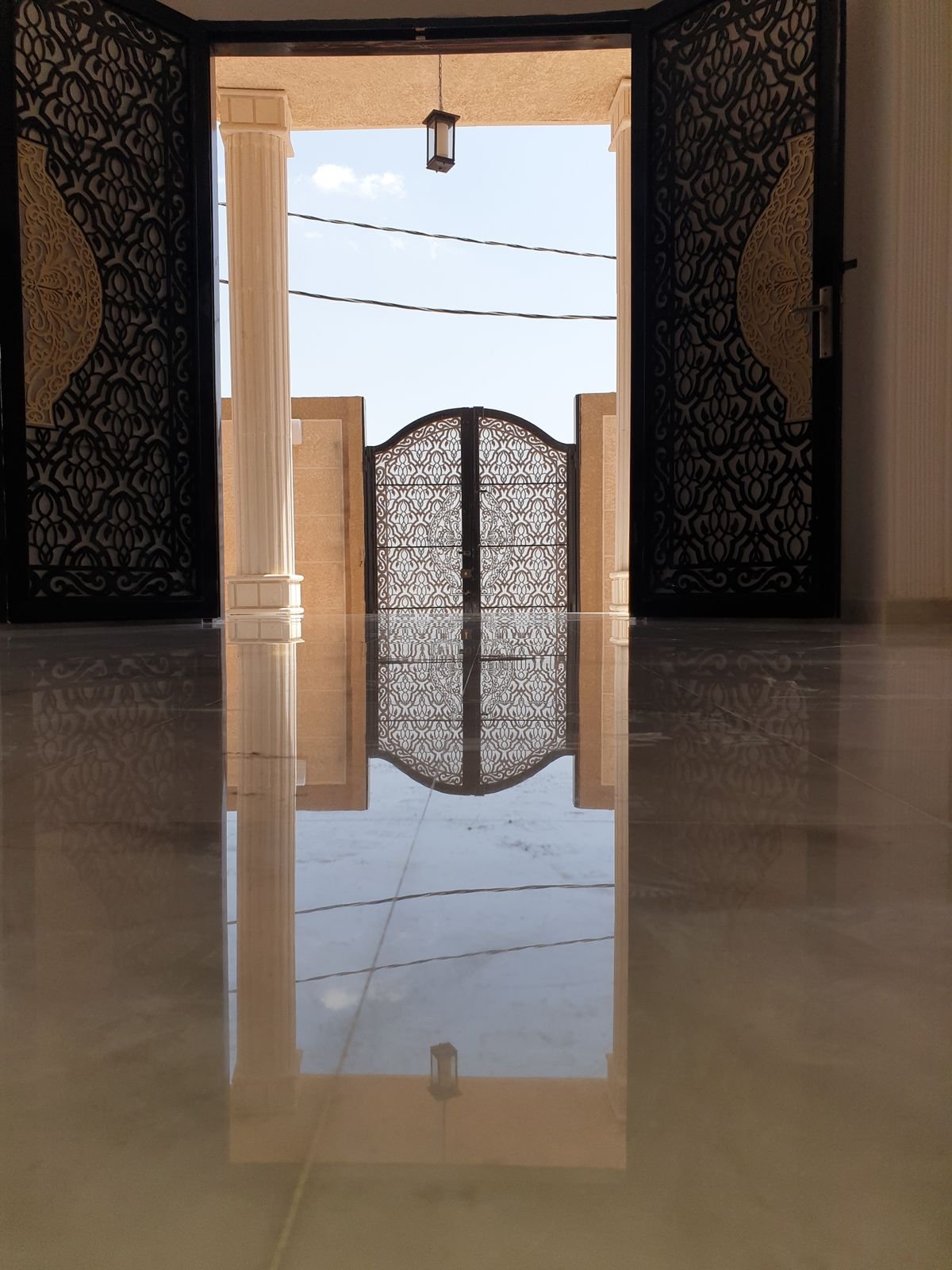 مدخل خارجي بين أعمدة بلون حجري وبوابة معدنية وأرضية لامعة